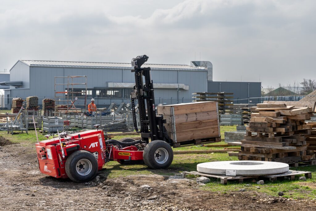 Autonomer Gabelstapler in rot mit AIT Logo legt Palette auf einer Baustelle ab.
